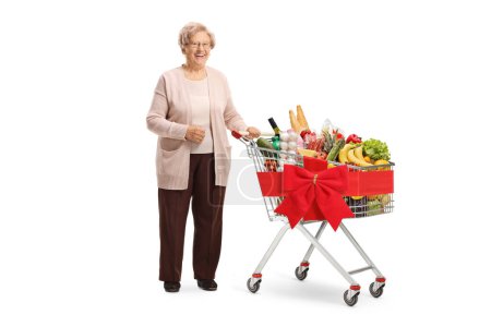 Téléchargez les photos : Femme âgée posant avec un panier attaché avec un ruban rouge et plein de nourriture isolée sur fond blanc - en image libre de droit