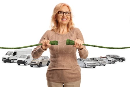 Photo for Middle aged woman plugging in green electric cables in front of vehicles isolated on white background - Royalty Free Image