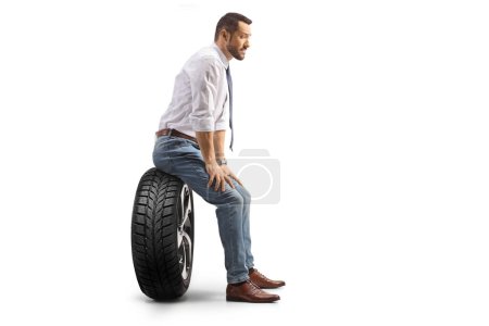 Téléchargez les photos : Plan du profil d'un homme assis sur un pneu de voiture et pensant isolé sur fond blanc - en image libre de droit