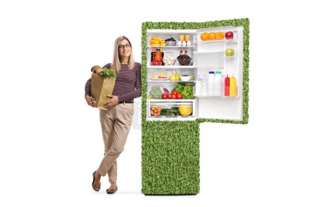 Téléchargez les photos : Jeune femme avec un sac d'épicerie appuyé sur un réfrigérateur vert avec des aliments sains isolés sur fond blanc - en image libre de droit