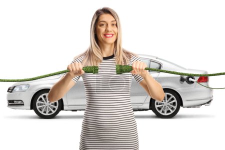 Foto de Mujer joven enchufando cables eléctricos verdes delante de un coche aislado sobre fondo blanco - Imagen libre de derechos