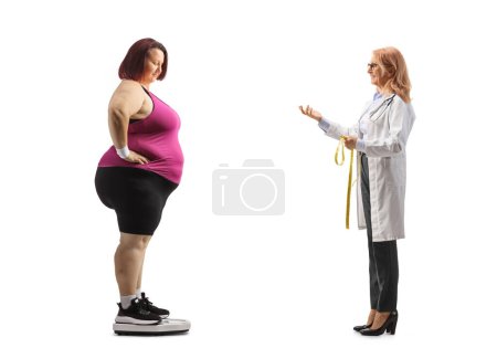 Téléchargez les photos : Plan de profil complet d'une femme médecin parlant à une femme corpulente dans une échelle de poids isolée sur fond blanc - en image libre de droit