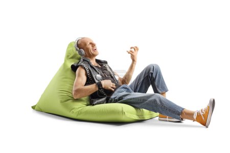 Bald punk man sitting on a green bean bag with headphones isolated on white background