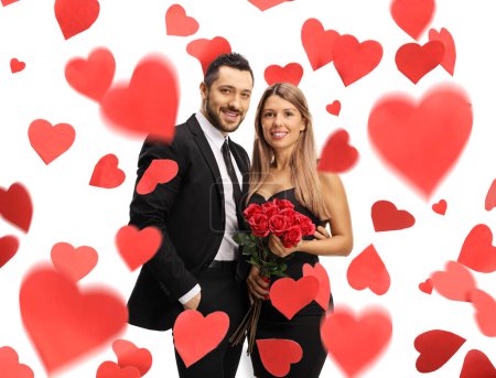 Téléchargez les photos : Jeune homme et femme avec des roses rouges debout sous des cœurs rouges isolés sur fond blanc - en image libre de droit
