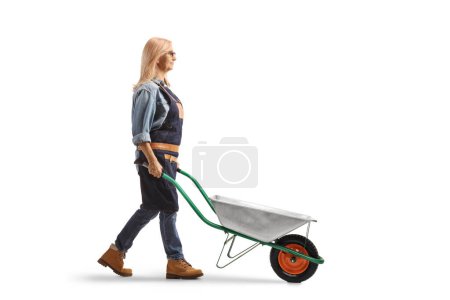 Photo for Full length profile shot of a female farmer pushing a wheelbarrow isolated on white background - Royalty Free Image