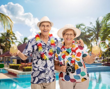 Photo for Elderly couple tourists with cocktails posing by a swimming pool - Royalty Free Image