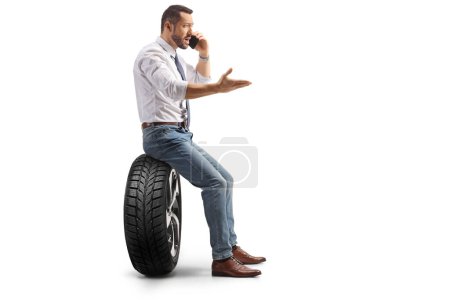 Photo for Profile shot of a businessman sitting on a car tire and using a smartphone isolated on white background - Royalty Free Image