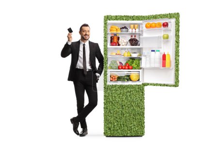 Téléchargez les photos : Homme d'affaires avec une carte de crédit appuyé sur un réfrigérateur vert isolé sur fond blanc - en image libre de droit