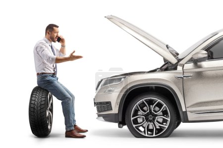 Téléchargez les photos : Profil d'un homme d'affaires avec un problème de voiture assis sur un pneu et appelant la société d'assistance routière isolé sur fond blanc - en image libre de droit