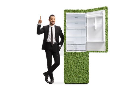 Téléchargez les photos : Directeur des ventes appuyé sur un réfrigérateur économe en énergie et pointant isolé sur fond blanc - en image libre de droit