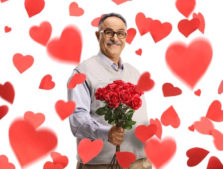 Foto de Hombre maduro sonriente sosteniendo un ramo de rosas rojas y de pie debajo de confeti en forma de corazón aislado sobre fondo blanco - Imagen libre de derechos