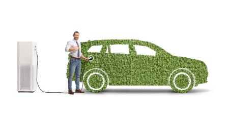 Téléchargez les photos : Homme d'affaires à une borne de recharge pointant vers un SUV électrique vert isolé sur fond blanc - en image libre de droit