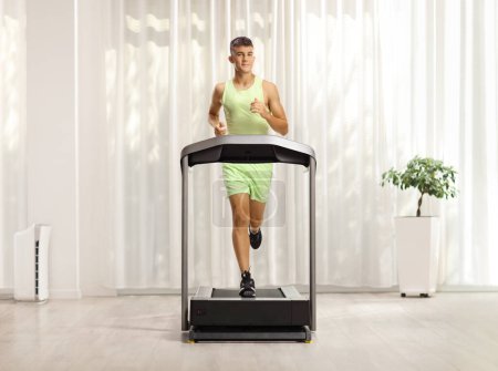 Photo for Teenage guy in sportswear running on a treadmill in a room - Royalty Free Image
