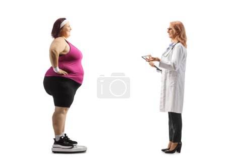 Photo for Female doctor talking to a corpulent woman in sportswear on a weight scale isolated on white background - Royalty Free Image