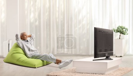 Téléchargez les photos : Afro-Américain assis sur un fauteuil sac de haricots verts et regarder la télévision dans un salon minimaliste moderne - en image libre de droit