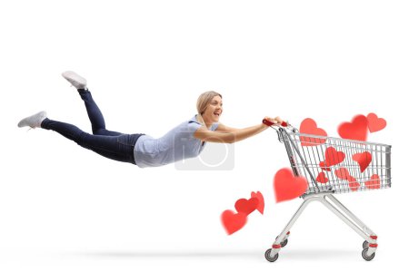 Photo for Excited woman in air holding a shopping cart with red hearts isolated on white background - Royalty Free Image
