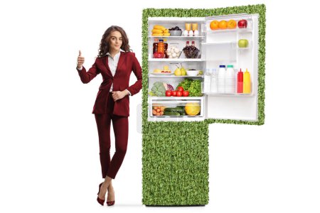 Sales woman with a green efficient fridge gesturing thumbs up isolated on white background