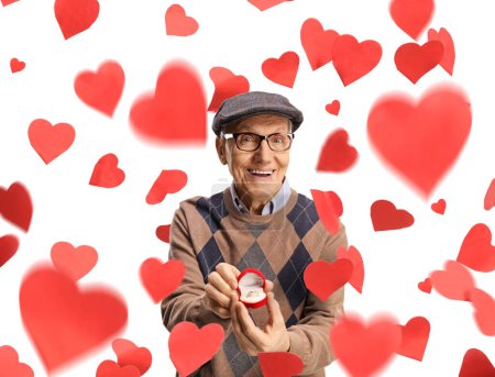 Téléchargez les photos : Homme âgé montrant une bague de fiançailles dans une boîte et debout sous des coeurs rouges isolés sur fond blanc - en image libre de droit