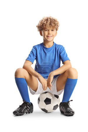 Photo for Happy boy in a sport jersey sitting on a football isolated on white background - Royalty Free Image