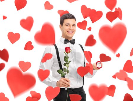 Téléchargez les photos : Jeune homme sous les coeurs tenant une rose et une bague de fiançailles isolée sur fond blanc - en image libre de droit
