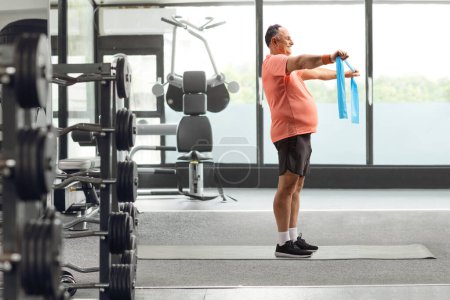 Téléchargez les photos : Plan de profil complet d'un homme mature en vêtements de sport faisant de l'exercice avec une sangle extensible dans une salle de gym - en image libre de droit