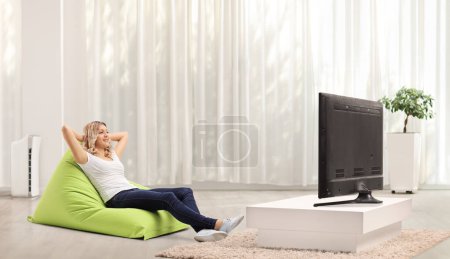 Téléchargez les photos : Jeune femme assise sur une chaise verte et relaxante devant la télé - en image libre de droit