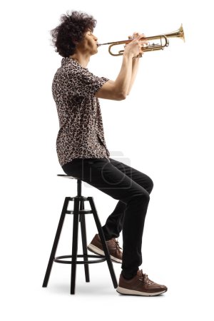 Téléchargez les photos : Artiste masculin assis sur une chaise et jouant une trompette isolée sur fond blanc - en image libre de droit