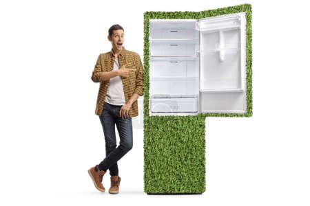 Photo for Casual man in shirt and jeans leaning on a green eco-friendly fridge and pointing isolated on white background - Royalty Free Image