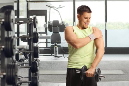 Téléchargez les photos : Homme avec blessure à l'épaule soulevant des poids dans une salle de gym - en image libre de droit