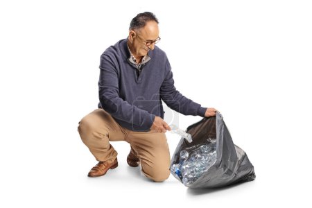Téléchargez les photos : Mature homme collecte des bouteilles en plastique dans un sac poubelle noir isolé sur fond blanc - en image libre de droit
