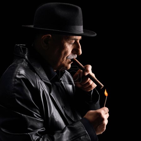 Photo for Profile shot of a mature man lighting a cigar isolated on black background - Royalty Free Image