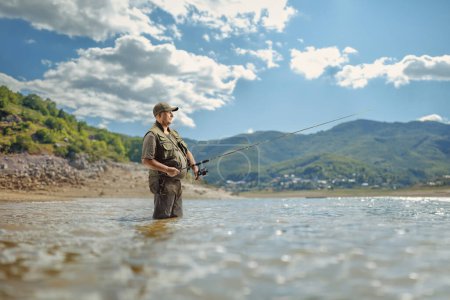 Pescador con caña de pescar dentro de un lago de montaña, Mavrovo, Macedonia