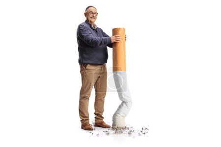 Téléchargez les photos : Portrait pleine longueur d'un homme mûr heureux repoussant une grosse cigarette isolée sur fond blanc, abandonner le concept de fumer - en image libre de droit