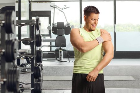 Téléchargez les photos : Homme dans une salle de gym, tenant son épaule douloureuse, concept de blessure sportive - en image libre de droit