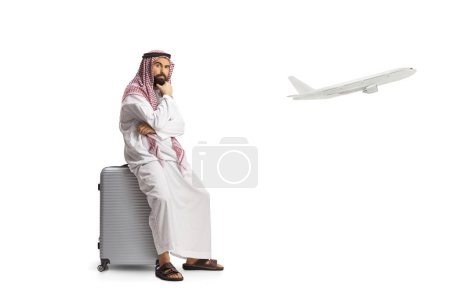 Photo for Saudi arab man sitting on a suitcase and waiting for a delayed flight isolated on white background - Royalty Free Image