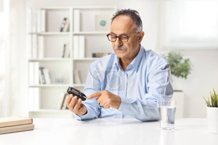 Photo for Mature man using a glucose monitor for blood sugar level - Royalty Free Image
