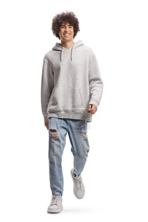 Photo for Full length portrait of a cute tall guy with curly hair in a gray hoodie and jeans walking towards camera isolated on white background - Royalty Free Image