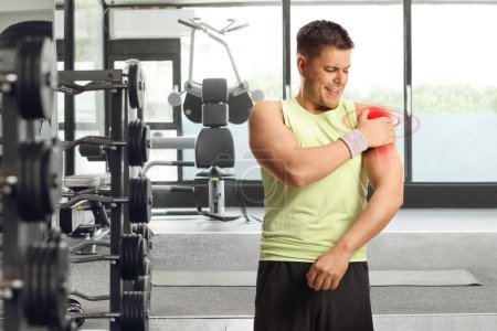 Téléchargez les photos : Homme dans une salle de gym, tenant son épaule rouge douloureuse, concept de blessure sportive - en image libre de droit