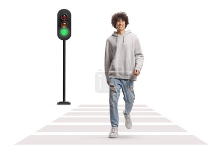 Téléchargez les photos : Grand gars aux cheveux bouclés dans un sweat à capuche gris et un jean marchant à un passage pour piétons isolé sur fond blanc - en image libre de droit