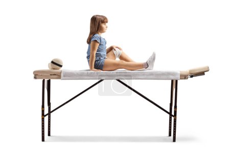 Photo for Full length profile shot of a child with leg injury sitting on a phycical therapy bed isolated on white background - Royalty Free Image