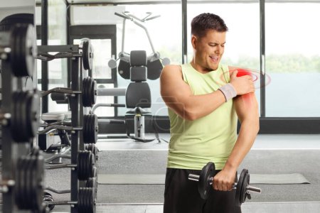 Foto de Hombre haciendo ejercicio en un gimnasio y sosteniendo su hombro doloroso rojo, concepto de lesiones deportivas - Imagen libre de derechos