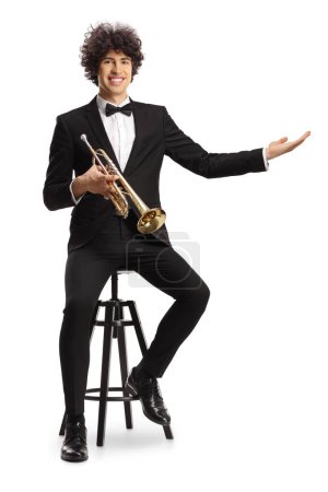 Photo for Smiling young male musician in a black suit holding a trumpet welcoming with hand isolated on white background - Royalty Free Image