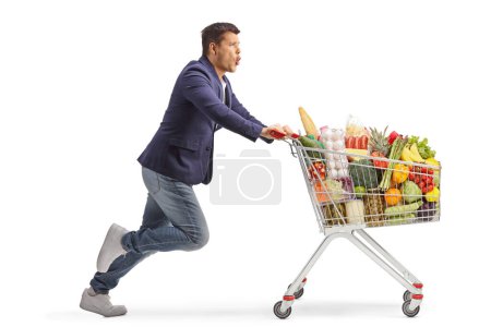 Téléchargez les photos : Photo de profil pleine longueur d'un homme excité courant avec un chariot de supermarché isolé sur fond blanc - en image libre de droit