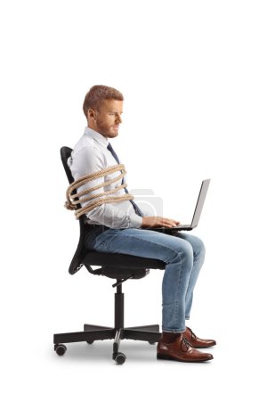 Foto de Perfil de un trabajador de oficina sentado en una silla atado con una cuerda y trabajando en un ordenador portátil aislado sobre fondo blanco - Imagen libre de derechos