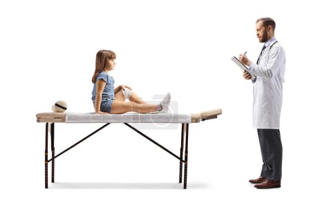 Téléchargez les photos : Physiothérapeute et une petite fille blessée à la jambe assise sur un lit thérapeutique isolé sur fond blanc - en image libre de droit