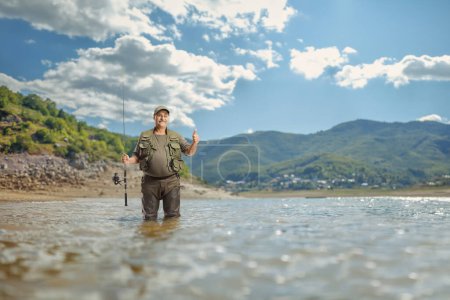 Foto de Pescador en un lago de pie con una caña de pescar y mostrando los pulgares hacia arriba - Imagen libre de derechos
