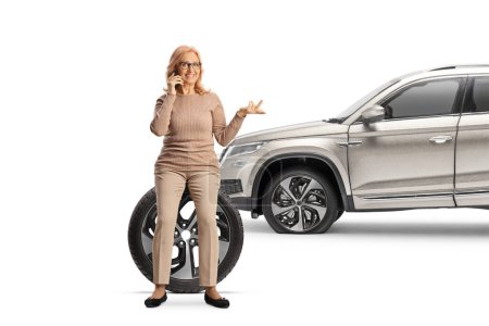 Téléchargez les photos : Femme avec un 4x4 assis sur un pneu de voiture et utilisant un smartphone isolé sur fond blanc - en image libre de droit