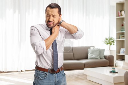 Foto de Hombre con dolor sosteniendo su cuello inflamado en una sala de estar - Imagen libre de derechos