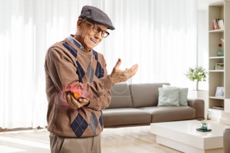 Elderly man in pain holding elbow at home in a living room
