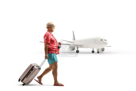 Foto de Plano de perfil de longitud completa de un turista varón maduro con pasaporte y tirando de una maleta en el aeropuerto aislado sobre fondo blanco - Imagen libre de derechos